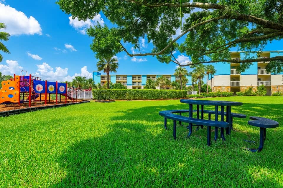 Grassy recreation area with playground equipment, picnic table, and apartment buildings