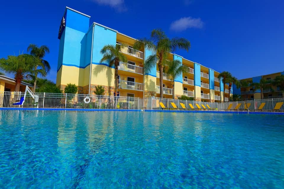 Colorful apartment complex with blue and yellow facade overlooking crystal clear swimming pool under blue sky
