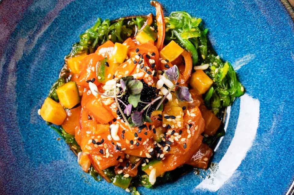 Vibrant Asian-inspired dish with glazed protein, colorful peppers, sesame seeds, and microgreens on blue plate