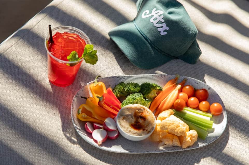 Healthy poolside lunch with fresh vegetable platter, hummus, red drink, and resort cap on lounge chair