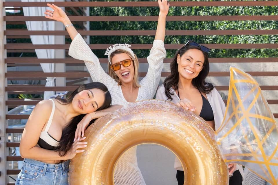 Three women posing with gold inflatable ring float at poolside lounge area