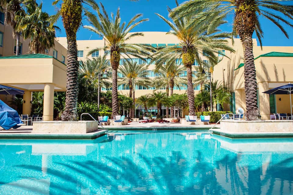 Resort pool with crystal-clear turquoise water, palm trees, and multi-story beige hotel building