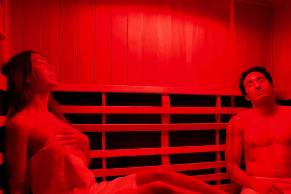 Red infrared sauna room with two people relaxing on wooden benches
