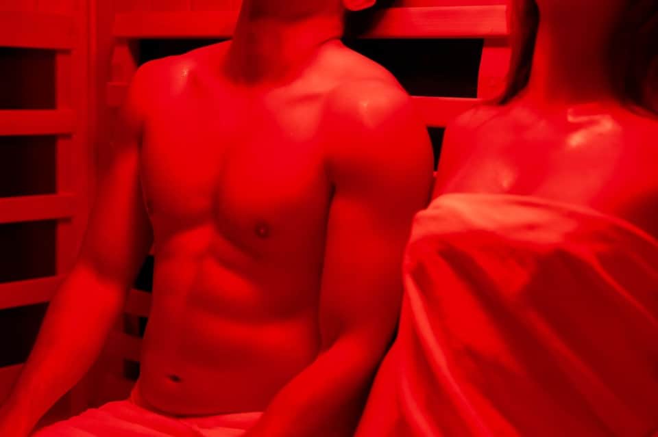 Close-up of two people in red infrared sauna with geometric wall pattern