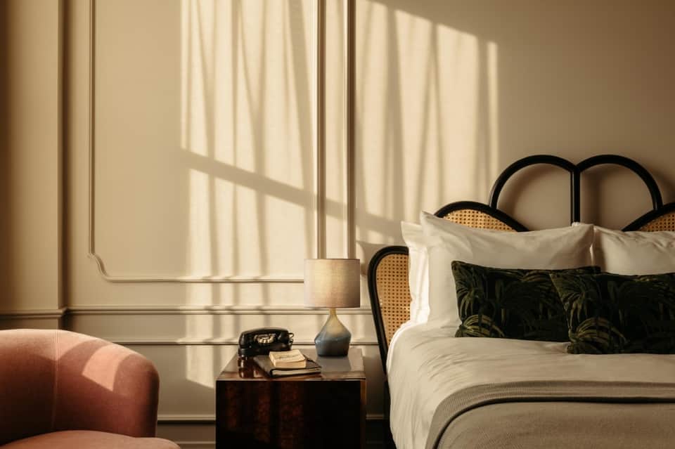 Luxury bedroom with sunlit windows, cream curtains, black headboard bed, and minimalist decor