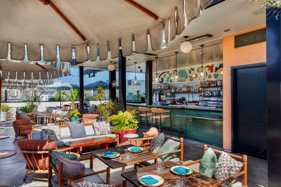 Modern rooftop bar lounge with orange accents, geometric pendant lights, bar counter, and city views