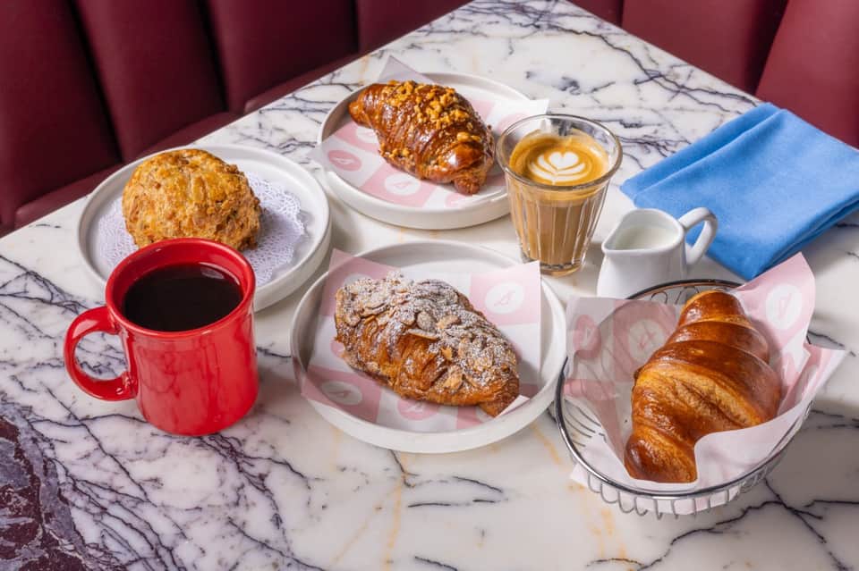 Marble table with pastries, croissants, coffee in red mug, cappuccino, and blue linen napkin