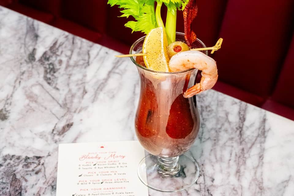 Bloody Mary cocktail with shrimp and celery garnish on marble table with menu card