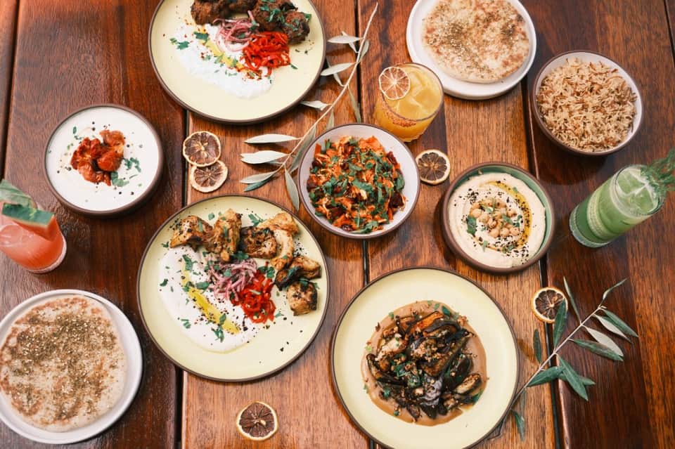 Overhead view of plated Mediterranean dishes with hummus, grilled vegetables, and fresh drinks