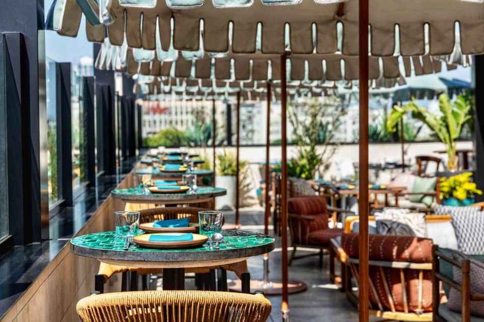 Outdoor dining terrace with turquoise table settings, pergola shade, and palm tree views