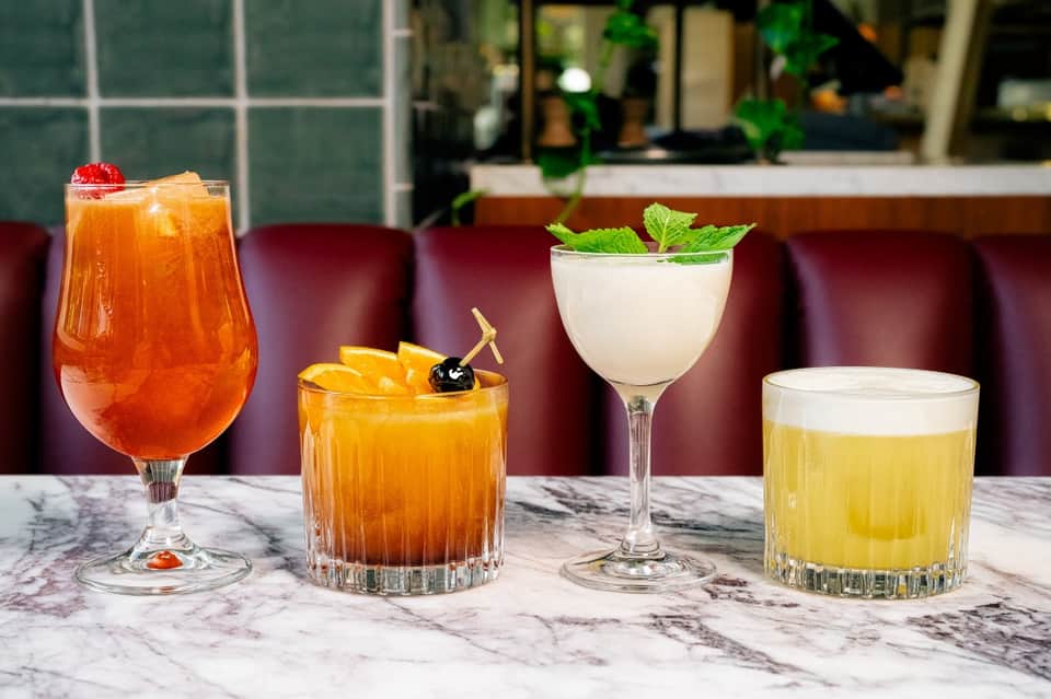 Four colorful cocktails on a marble countertop: tropical, old fashioned, mojito, and martini