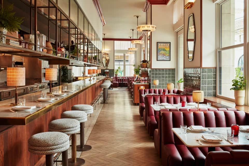 Upscale restaurant with burgundy banquettes, open kitchen, copper accents, and natural light