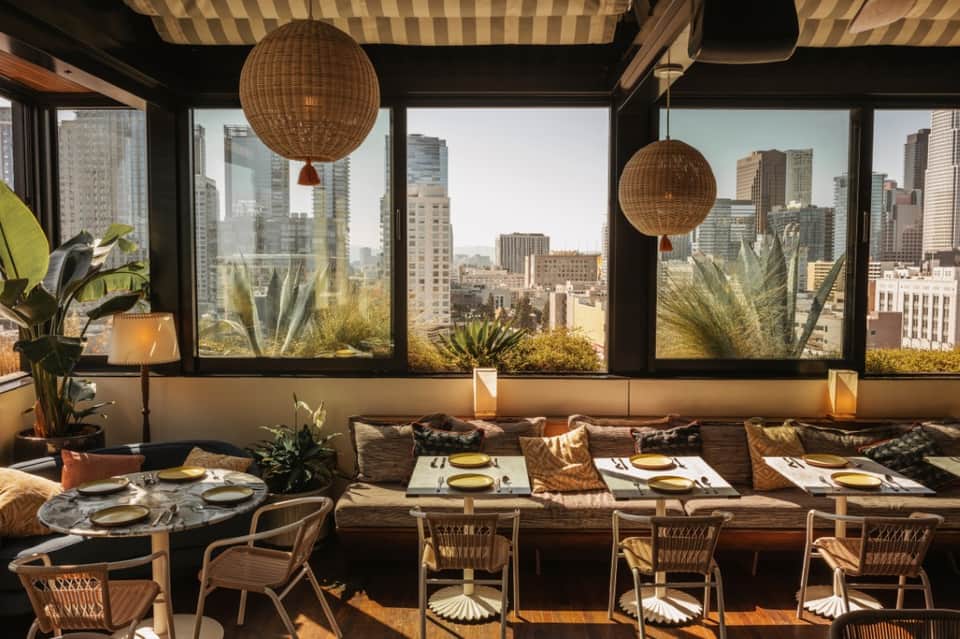 Upscale restaurant with city skyline views, woven pendant lights, booth seating, place settings, and modern furnishings