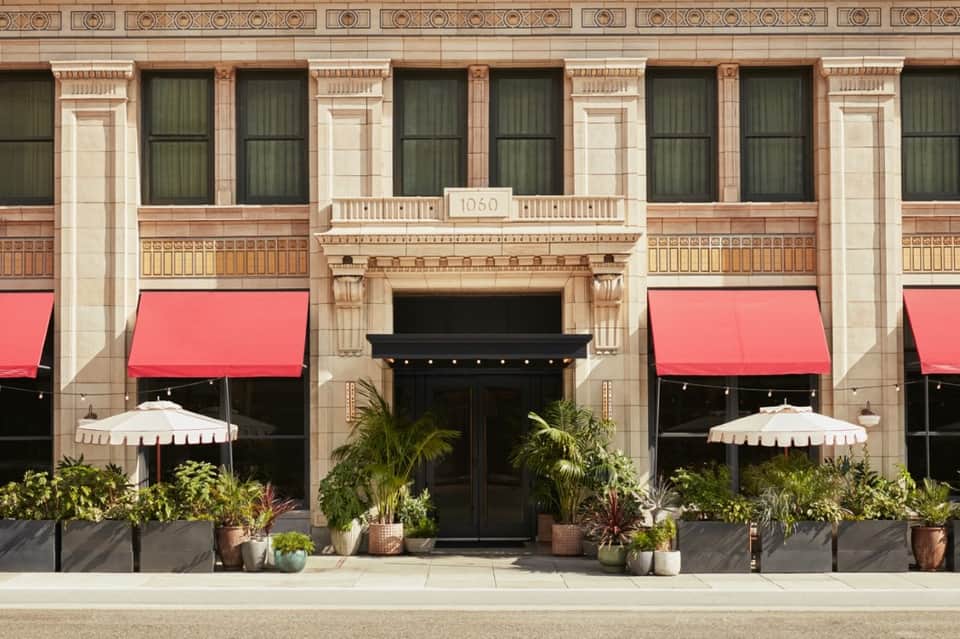 Historic hotel facade with ornate stonework, arched windows, red awnings, and potted plants