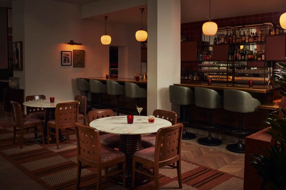 Sophisticated bar and lounge with marble cocktail tables, leather seating, pendant lights, and full-service bar