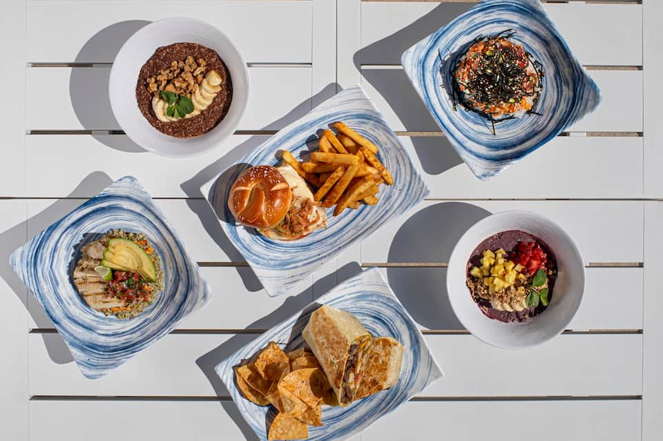 Overhead view of healthy food plates with bowls, burgers, fries, and fresh ingredients on white wooden table