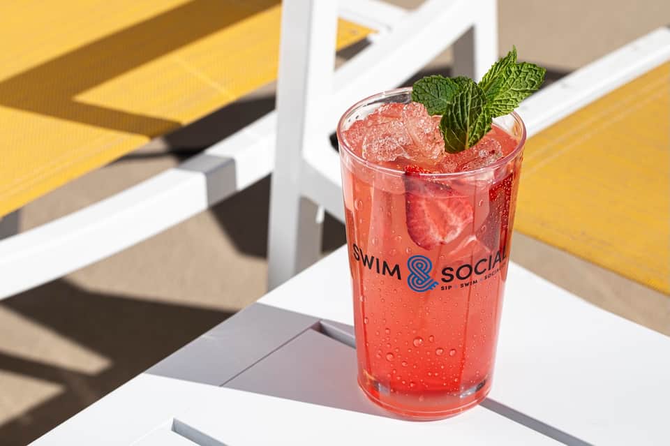 Refreshing pink cocktail with mint garnish at poolside bar with 'Swim & Social' branding