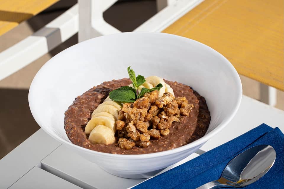 Gourmet chocolate risotto bowl topped with granola, banana slices, and mint garnish at dining table