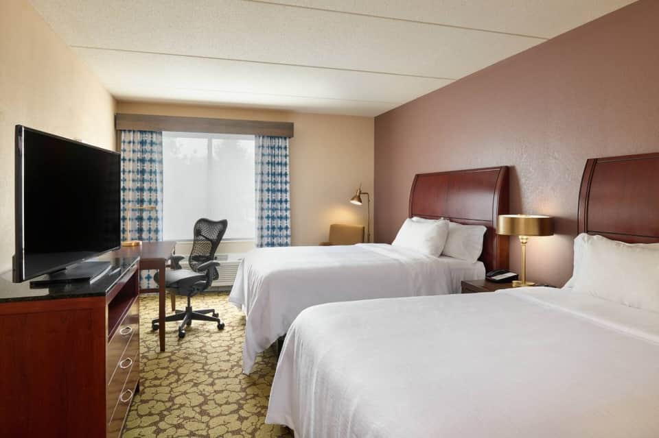 Double queen hotel room with burgundy walls, work desk, flat-screen TV, and blue patterned curtains