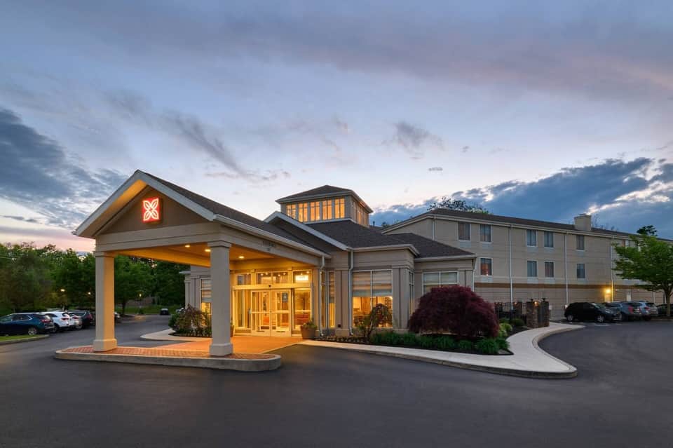 Hotel exterior at dusk with illuminated entrance portico, multi-story building, and parking area