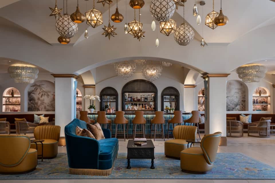 Elegant lobby lounge with ornate gold chandeliers, blue velvet chairs, and arched bar