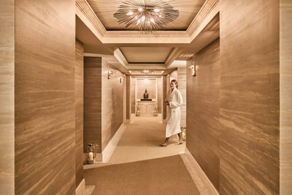 Luxury spa corridor with warm wood tones, coffered ceiling, decorative light fixture, and elegant design.