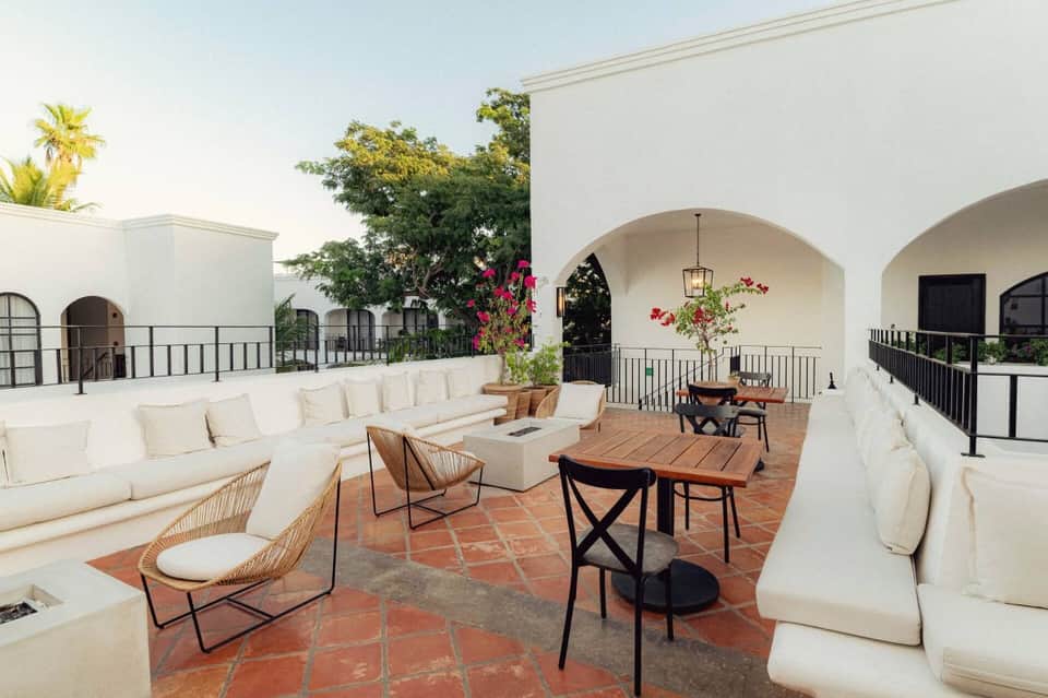 Rooftop terrace with cream-colored seating, arched white architecture, terra-cotta tile flooring, and flowering plants.