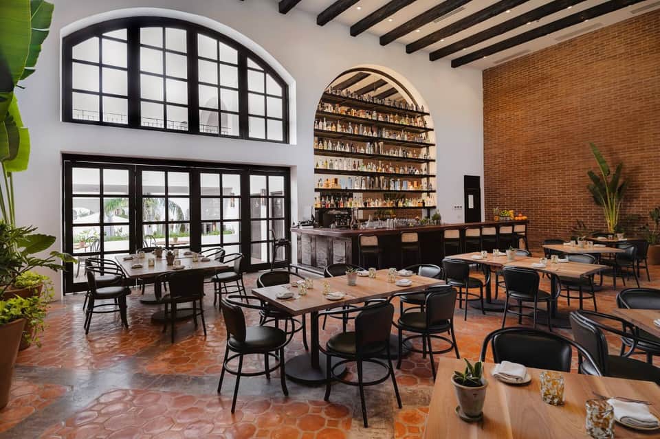 Modern restaurant interior with arched brick shelving, black-framed windows, exposed beams, and wooden dining tables.