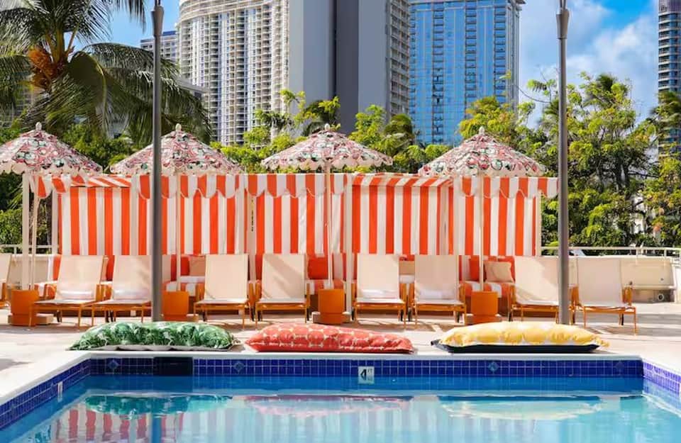 Resort pool with red and white striped umbrellas, lounge chairs, and high-rise buildings in background