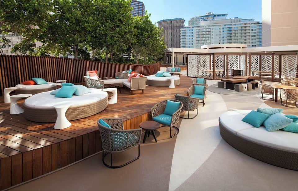 Urban rooftop terrace with curved loungers, modern furniture, wooden decking, and city skyline