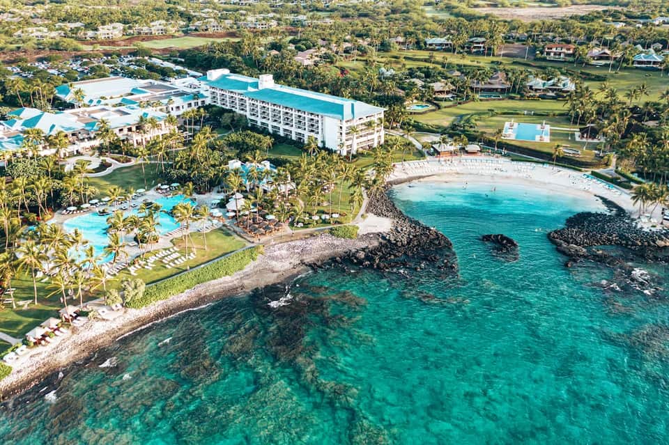 Beachfront resort aerial view with multiple pools, white buildings, tropical grounds, and pristine turquoise cove