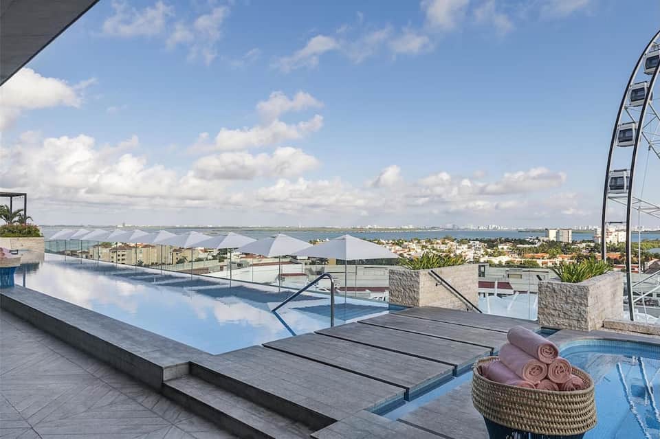 Infinity pool with ocean view, white umbrellas, and a Ferris wheel visible on the horizon