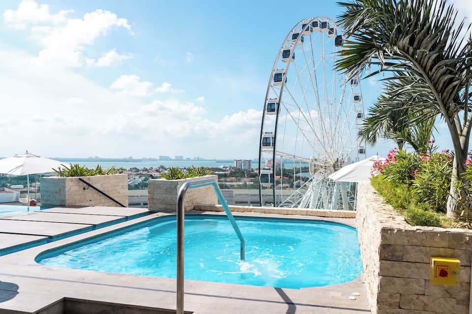 Rooftop pool with turquoise water overlooking a Ferris wheel and coastal cityscape under blue sky