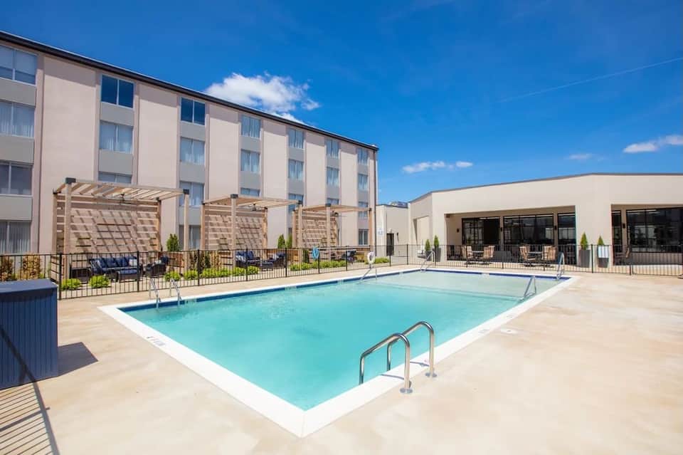 Daytime resort pool with pergolas, lounge seating, and hotel building under clear blue sky