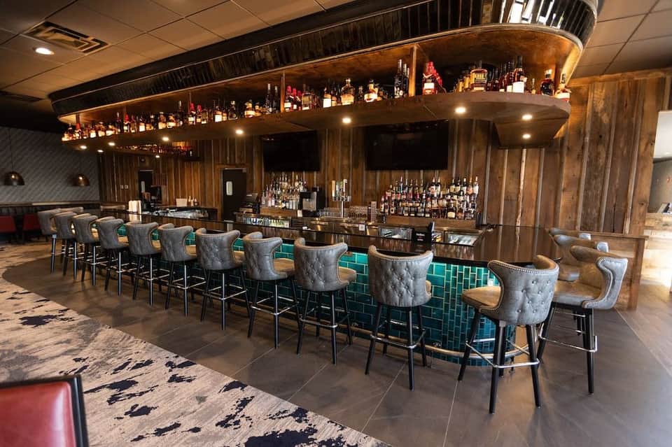 Upscale bar with wooden curved counter, bar seating, extensive liquor selection, and ambient lighting