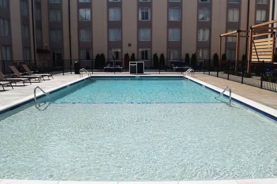 Hotel pool with shallow and deep sections, lounge chairs, and multi-story building backdrop