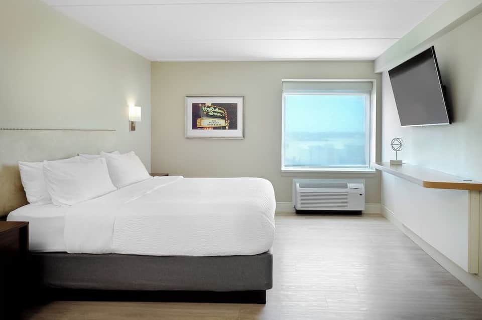 Spacious hotel room with single bed, TV, window with light control, and minimalist décor