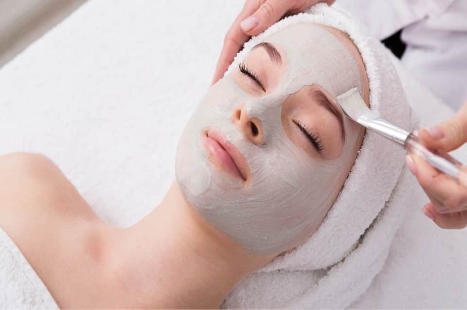 Facial spa treatment with therapist applying cream mask to woman's face