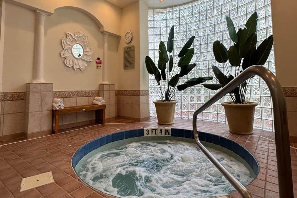 Indoor spa with hot tub at 3 ft 4 in depth, decorative mirror, potted plants, and glass block windows