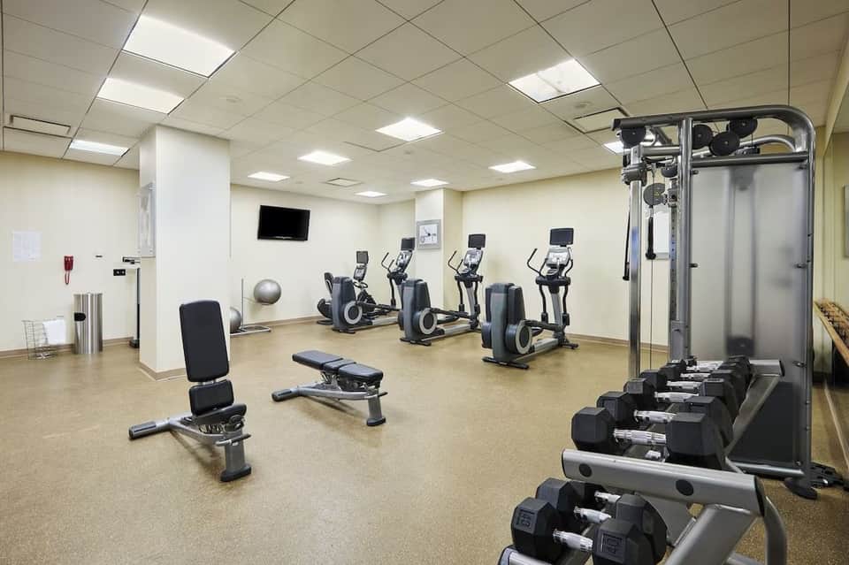Fitness center with cardio equipment, ellipticals, weight bench, dumbbells, and wall-mounted TV