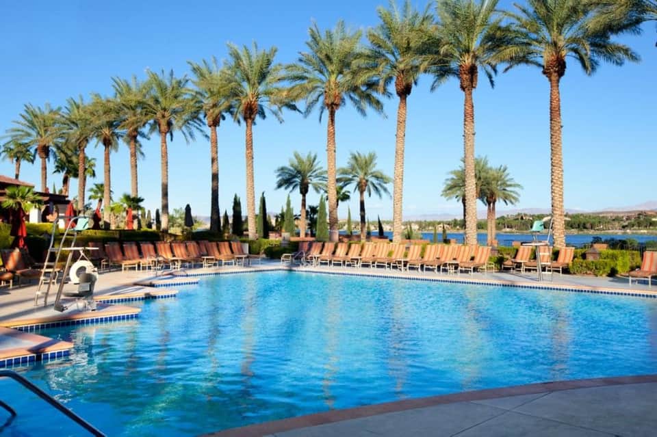 Large resort pool surrounded by tall palm trees, lounge chairs, and desert views