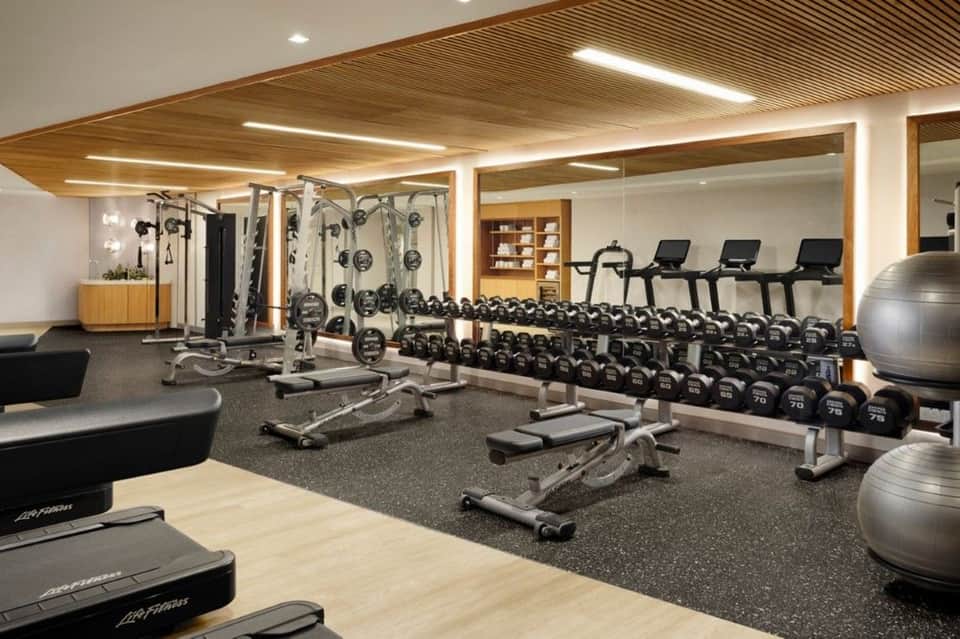 Modern fitness center with weight equipment, cardio machines, mirrors, and wooden ceiling