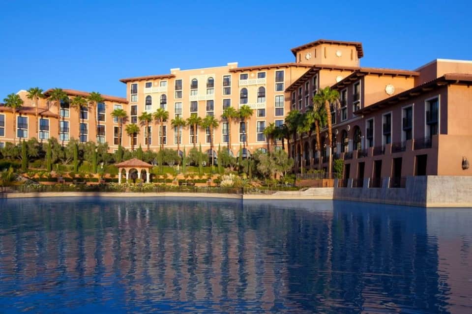 Mediterranean-style resort buildings reflected in calm water with palm trees lining waterfront