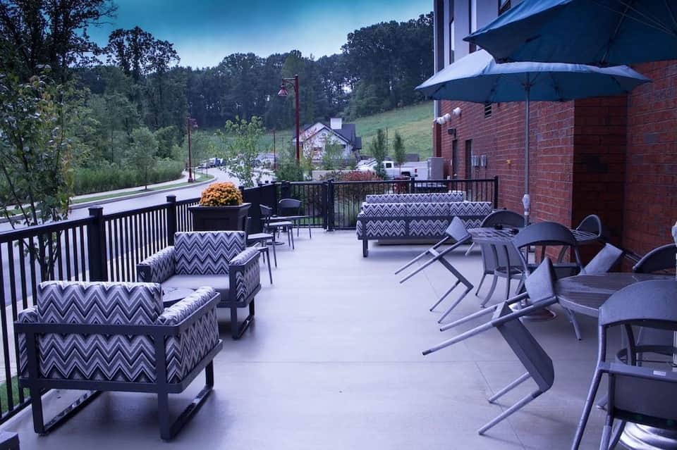Outdoor terrace with patio furniture, blue umbrella, black railings, and scenic hillside views