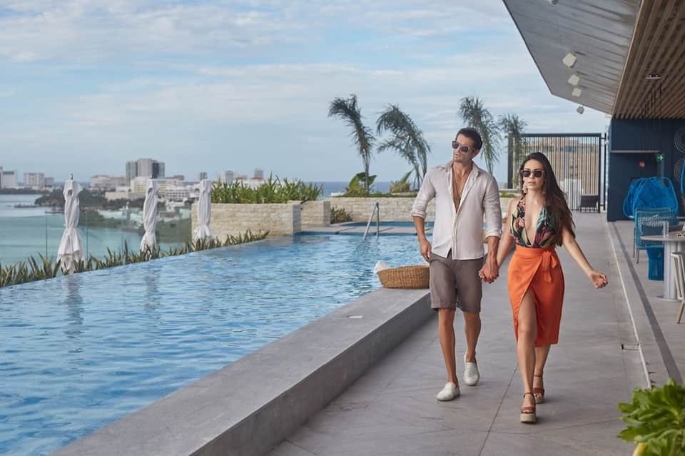Couple walking hand-in-hand along an infinity pool deck with city and ocean views