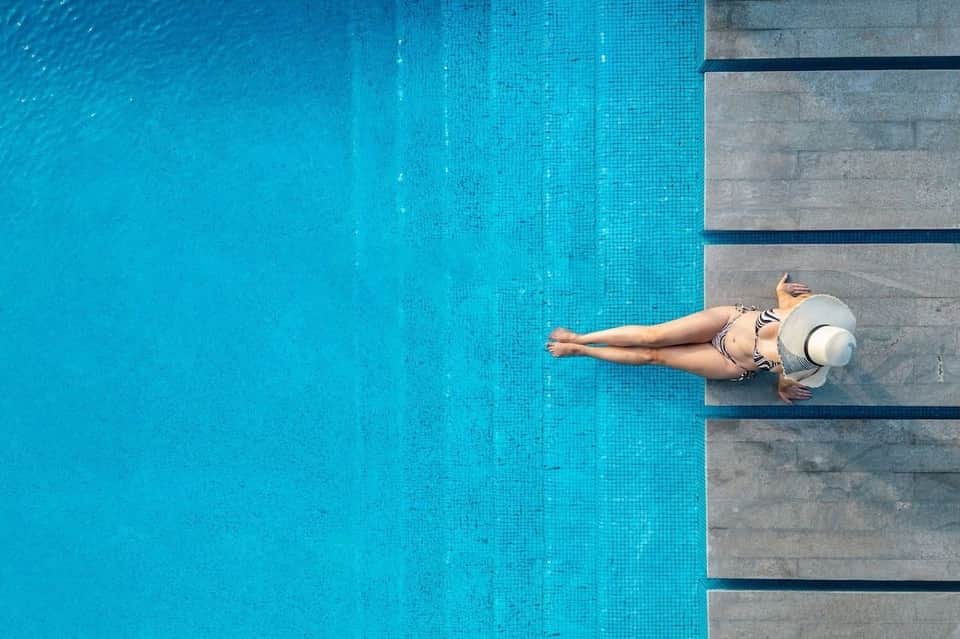 Woman in white hat lying poolside on concrete ledge next to bright turquoise water