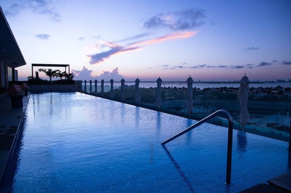Infinity pool at dusk with palm trees and white umbrellas overlooking bay