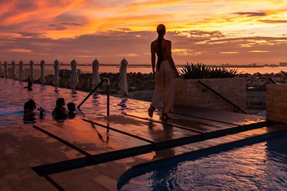 Woman in white dress at infinity pool during vibrant orange sunset