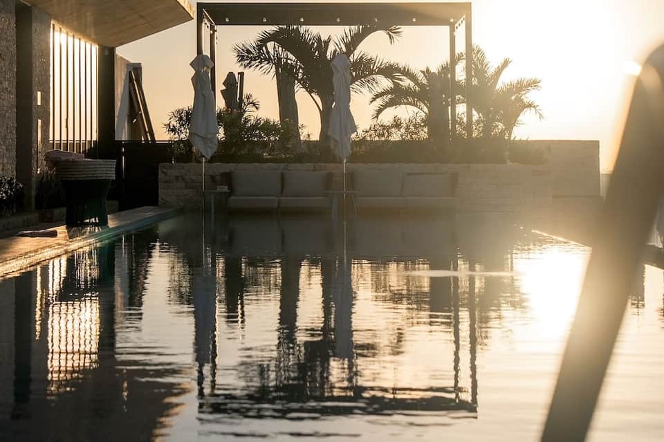 Luxury infinity pool at sunrise with palm tree reflections and modern architecture