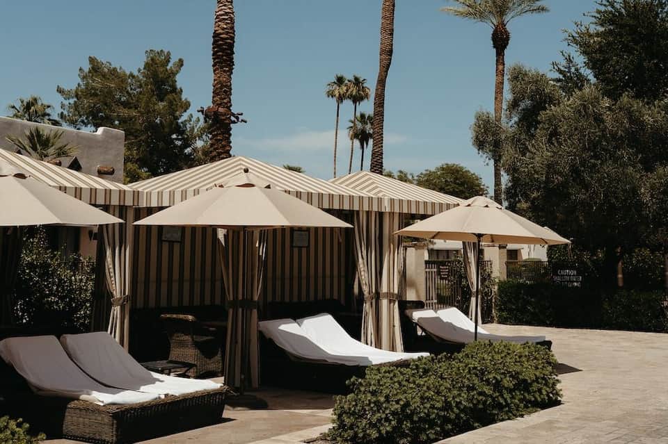 Striped cabanas with white loungers and umbrellas beside resort pool with palm trees